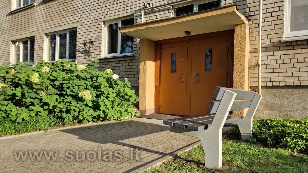 Pilkas betoninis lauko suolas su atlošu, pastatytas prie daugiabučio namo laiptinės